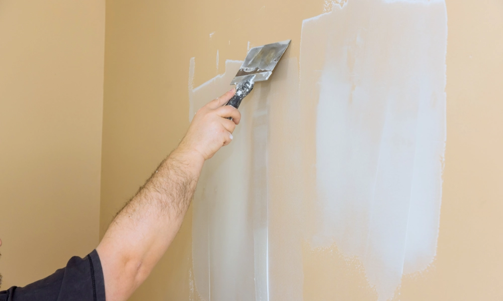 Person applying wall putty with a putty knife on a wall.