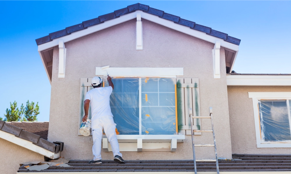 Painter in white outfit painting an exterior wall.