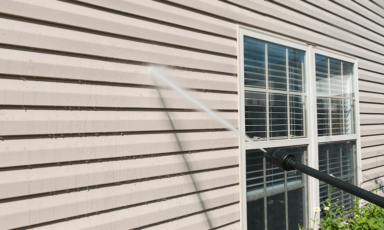 Pressure washing beige house siding next to a window.